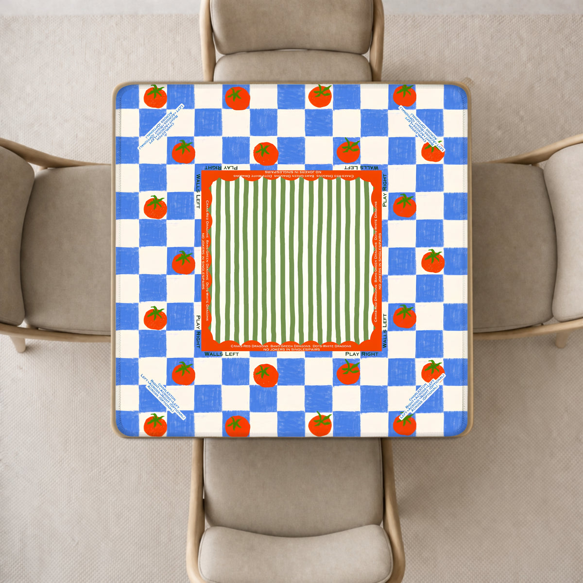 mahjong mat a colorful printed design, photographed from above in a dining room setting with four upholstered chairs around it. The mahjong mat design features a blue-and-white checkerboard border with small red tomatoesmotifs and a central green-and-white striped panel framed by red