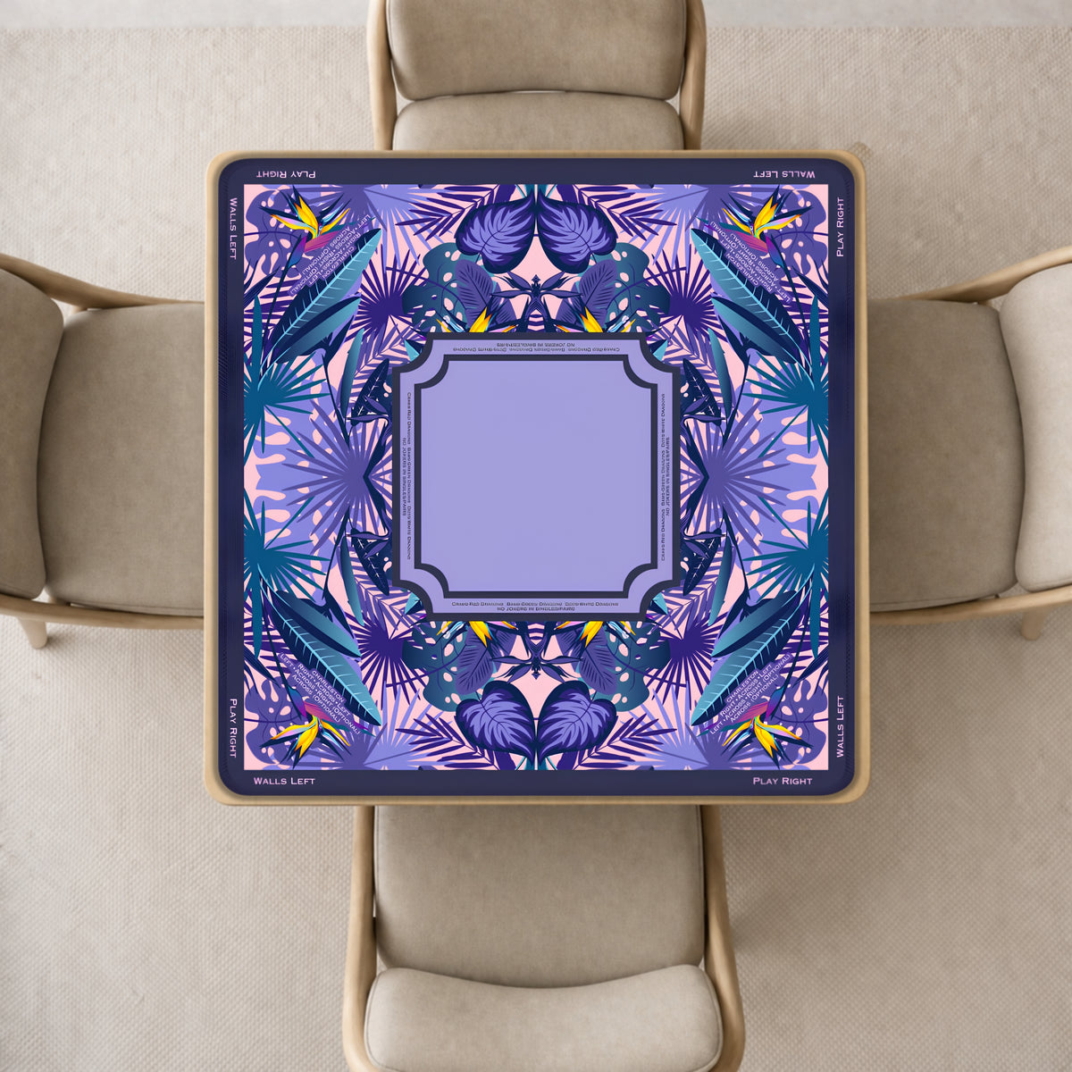 Mahjong mat with a decorative tropical design in shades of purple, blue, and pink, surrounded by four beige upholstered chairs in a neutral indoor setting.